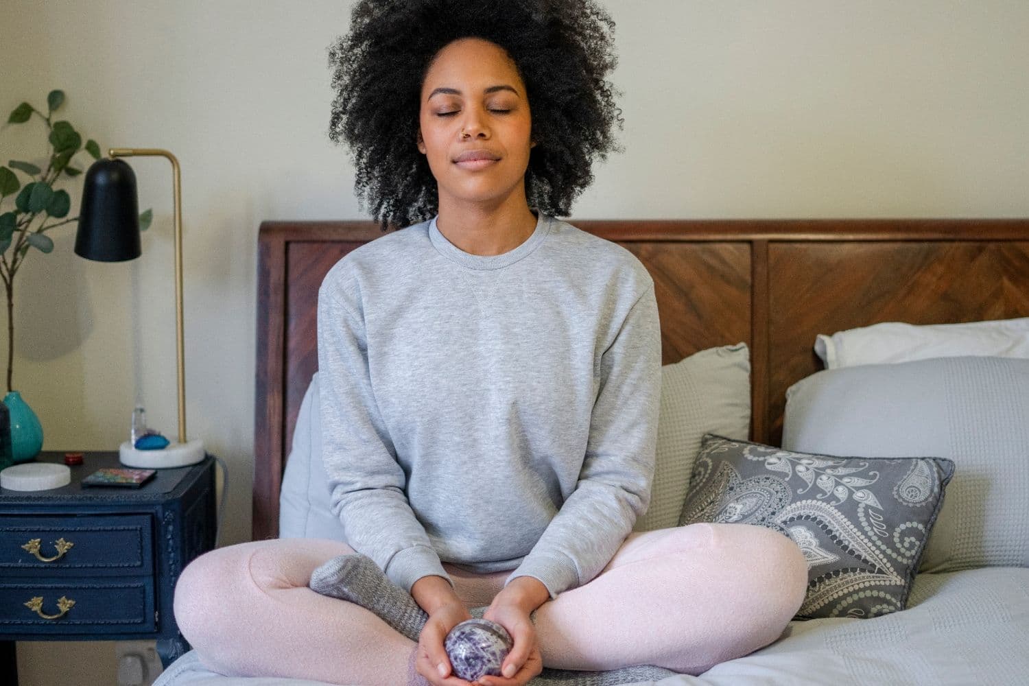 woman sitting on a bed with her eyes closed doing breathing exercises.