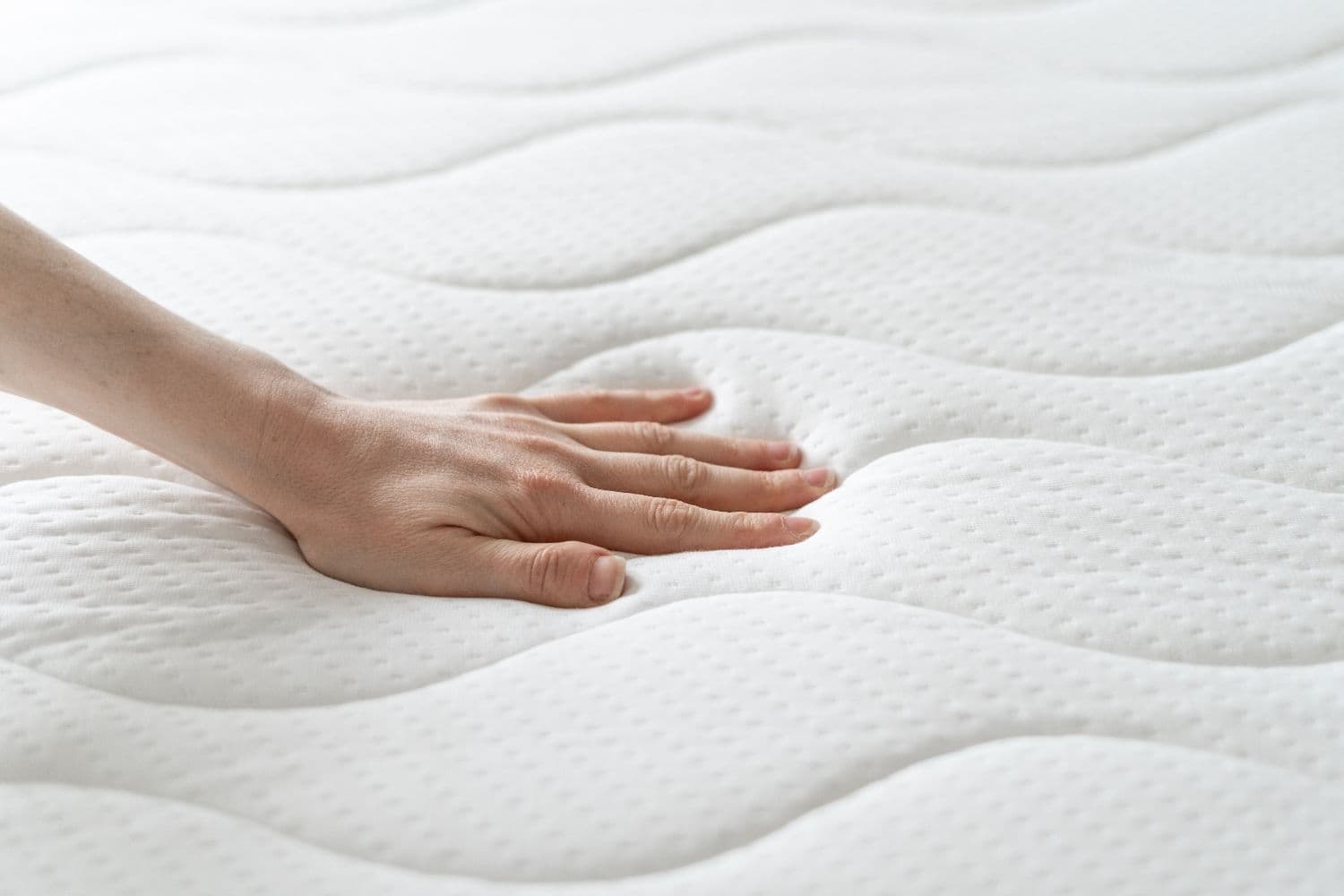 woman pushing down on a memory foam mattress with her hand. The mattress is white and has a wavey line pattern.