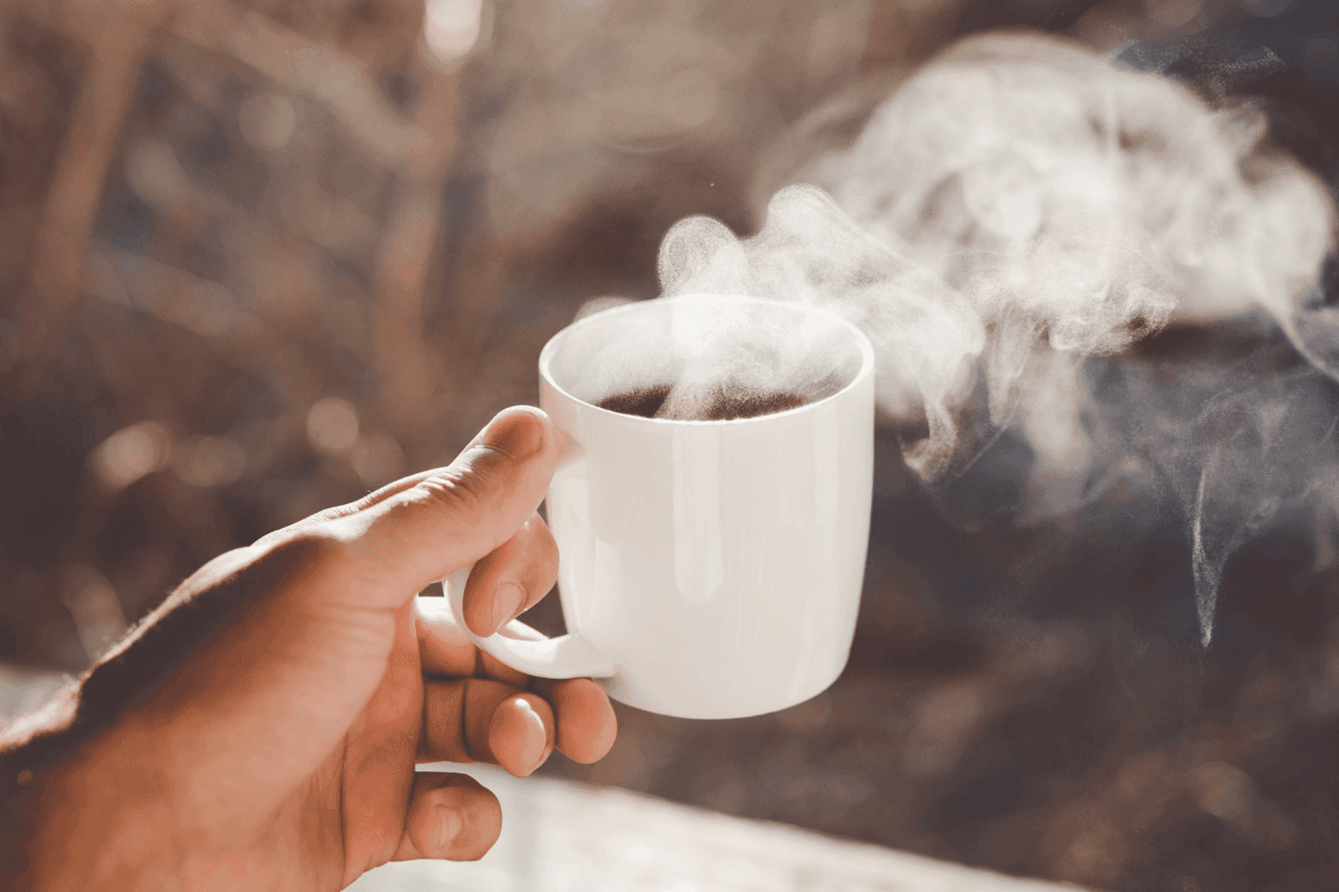hand holding hot drink outside with steam rising from the top