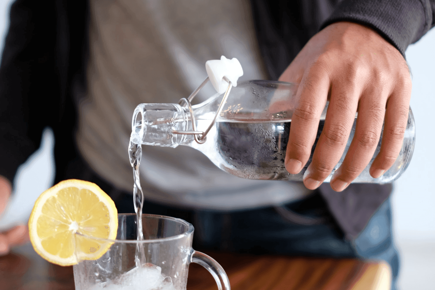 hand pouring bottle of water to a glass with a lemon wedge on.