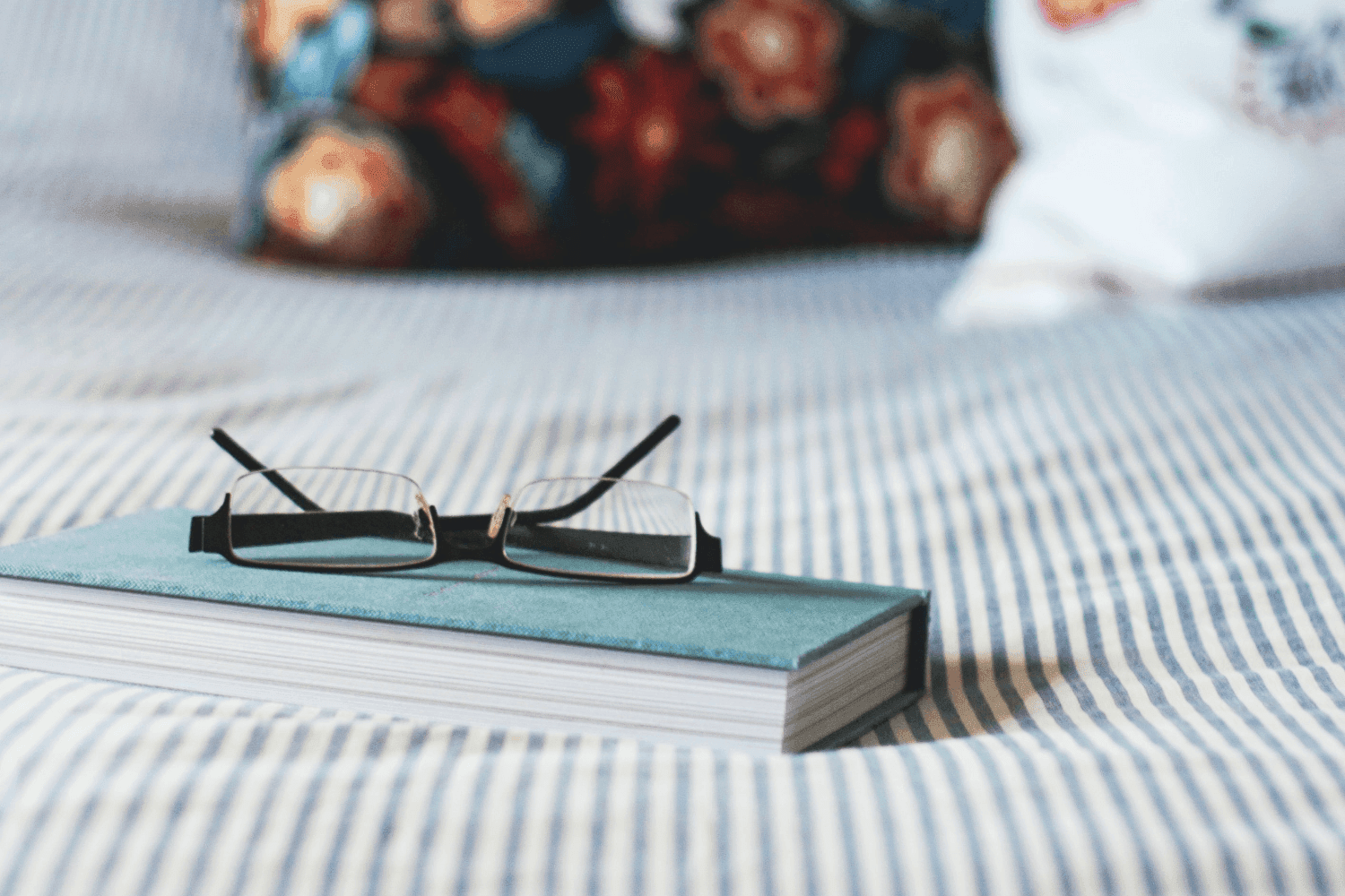 book on blue and white striped bed sheets with pair of glasses on top upside down