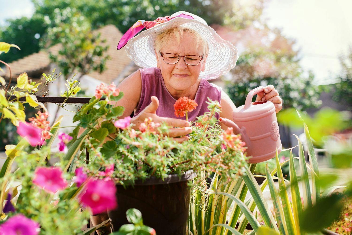 Woman wearing a pink top and hat gardening with a watering can