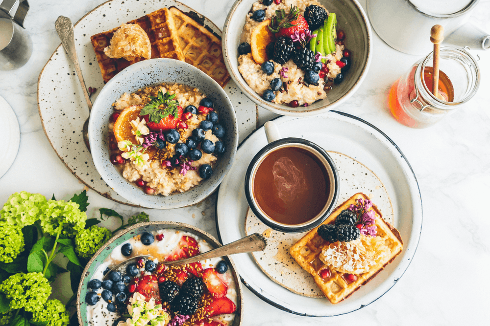 flatlay of breakfast foods with coffee, waffles, porridge and honey