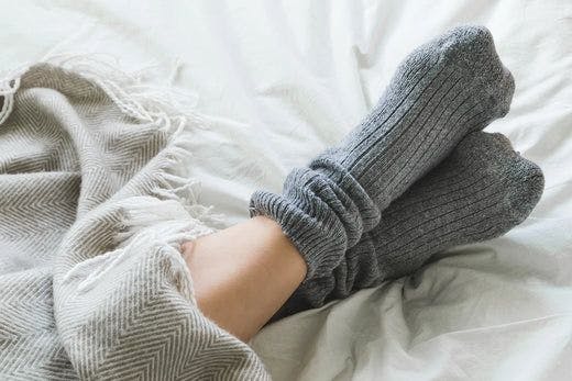Feet with grey socks on a bed with a blanket.