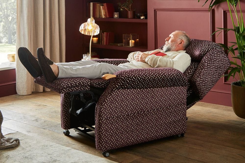 man in a beige loungewear set sleeping in a dark purple signature fabric rise and recline chair in a fully reclined position
