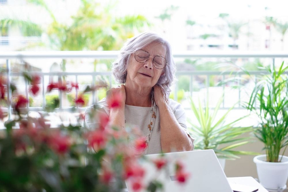 Older woman holding neck on balcony with expression of discomfort