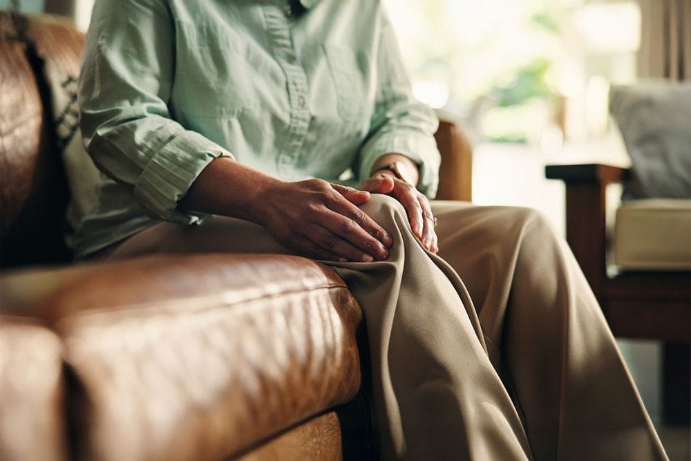 Older person holding their knee sat on sofa