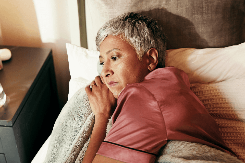Older woman with unhappy expression lying down in bed