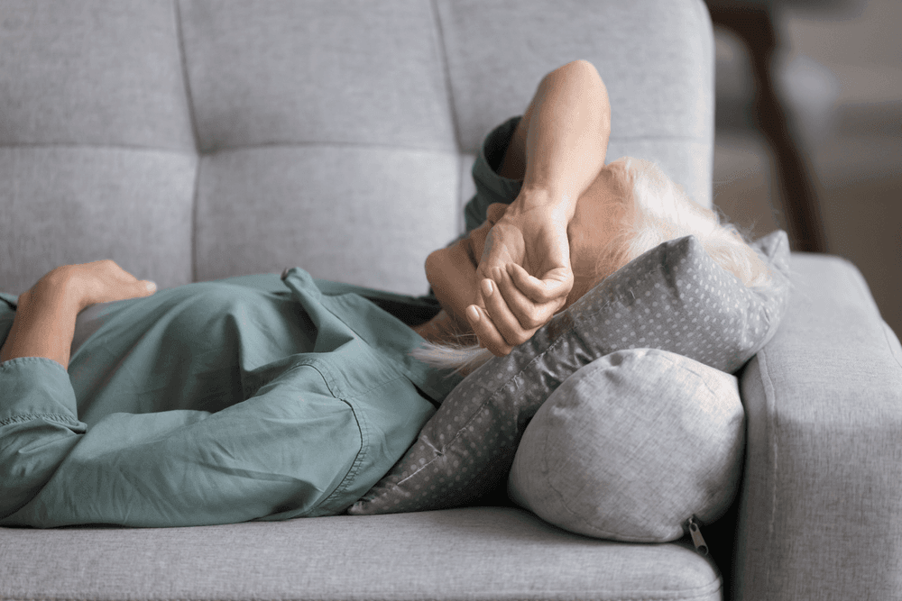 Older woman laying on sofa cushion with arm crossed over her face