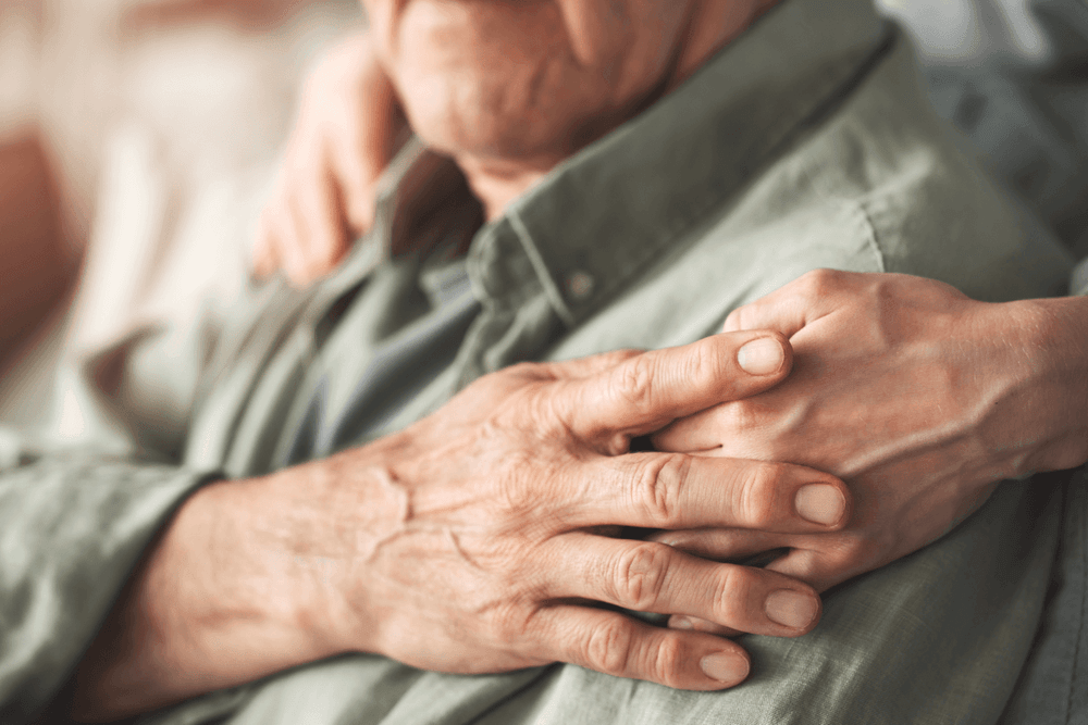 Focus on older mans shoulder where his hand is placed over the comforting hand of the person behind him