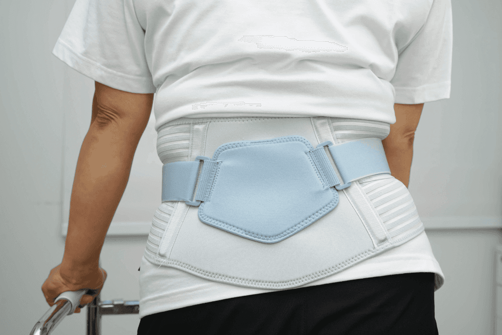 The back of an older woman in a white t-shirt wearing a white and blue lumbar support belt