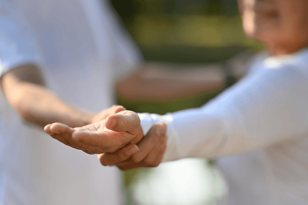 Close up of an instructor holding an older womans outstreched hand as she practises tai chi