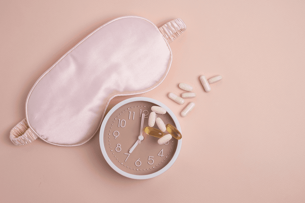 Pink sleeping mask next to a beside clock covered in natural supplements