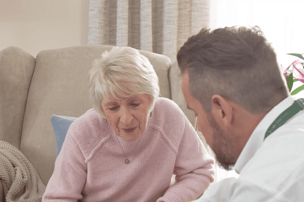 An older woman sat with an Oak tree rep discussing the chairs she'd like to try during her home appointment
