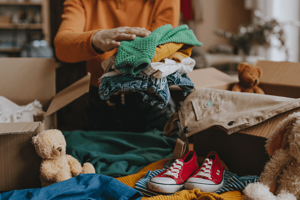 Close up of an older woman hands as she packs trousers, shirts, and teddy bears into cardboard boxes